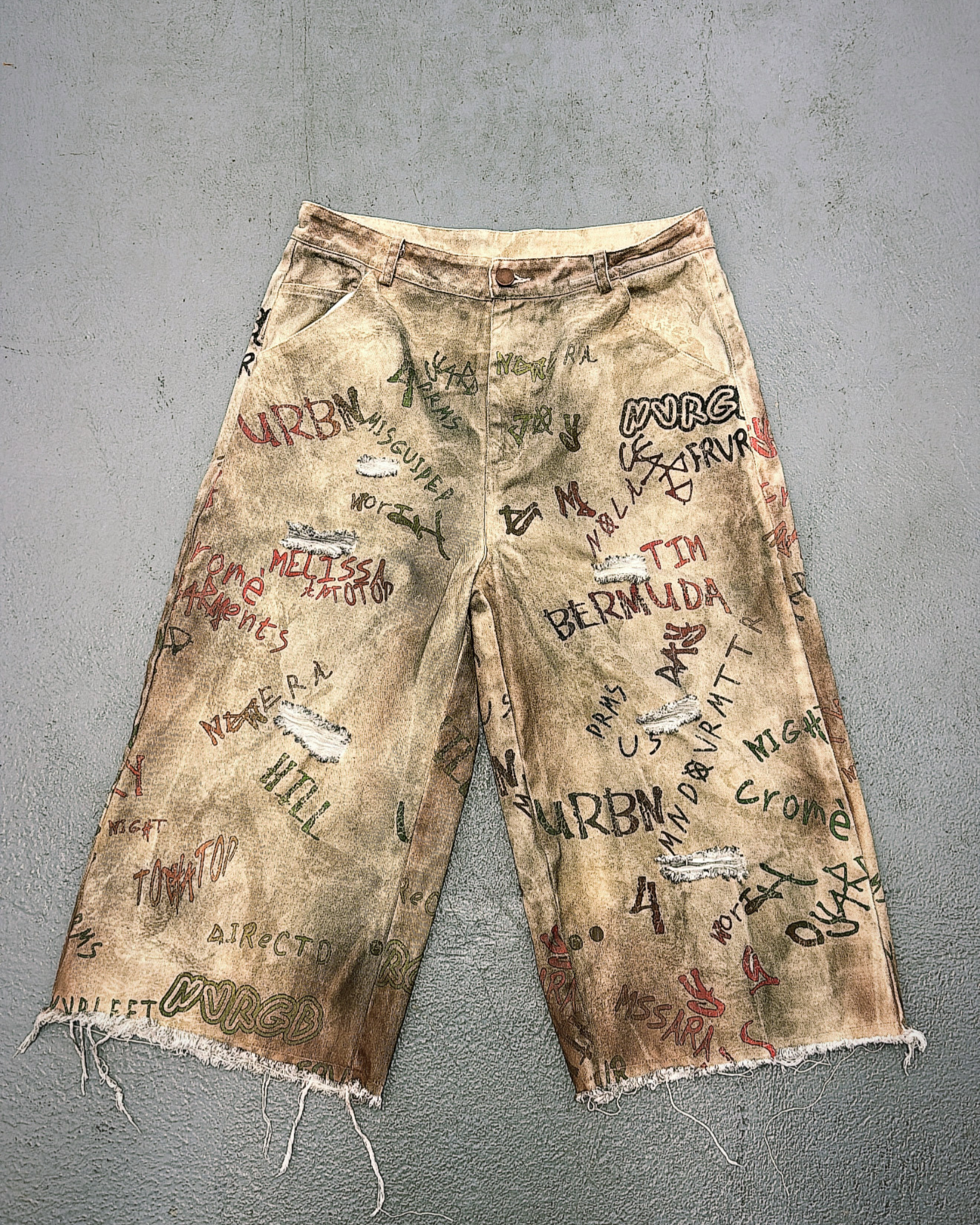 Distressed denim shorts with graffiti-style text on a gray background